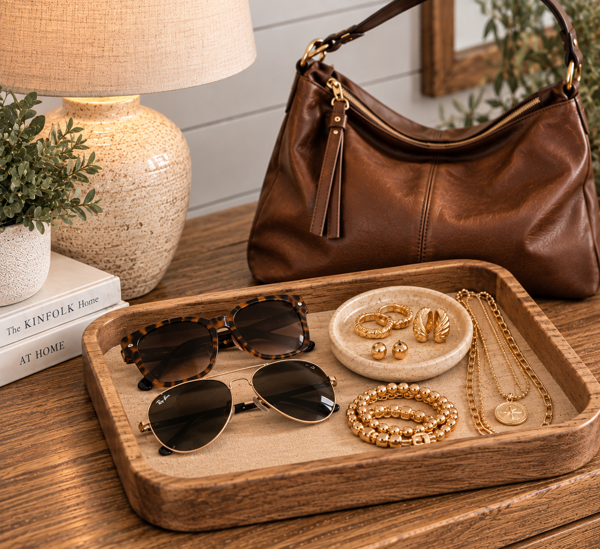 Handbag, sunglasses, and gold jewelry styled on a tray.