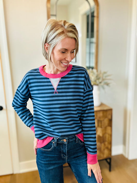 A woman wearing a blue and navy striped long-sleeve henley shirt with bright pink trim
